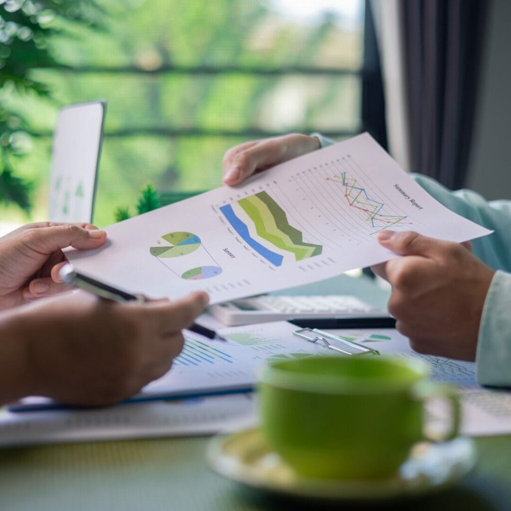 Image shows 2 people holding a tack of papers with reporting figures